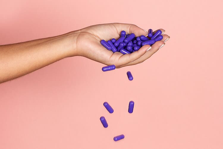 Mão feminina branca segura uma série de cápsulas de nutricosméticos, que podem ser aliados à saúde no combate aos danos causados por roer unhas.