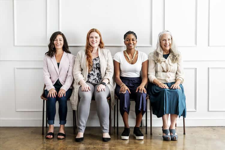 Quatro mulheres sentadas em um banco, uma ao lado da outra. Imagem para ilustrar conteúdo sobre Dia da Mulher.