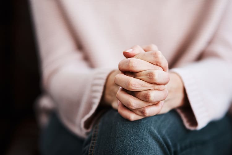 mulher segurando as mãos representando o que a ansiedade pode causar no corpo