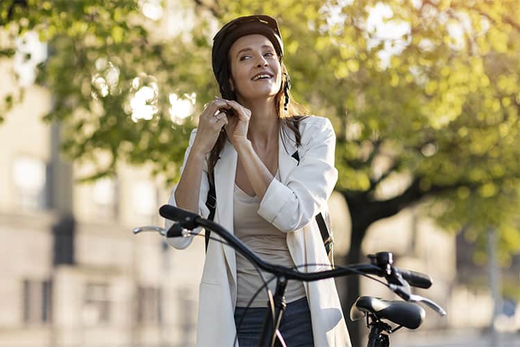 mulher colocando capacete representando quais são os benefícios de andar de bicicleta